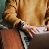 Persoon werkt op een laptop aan een houten tafel