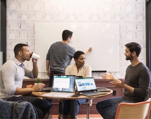 Vier collega’s overleggen rond laptops en een whiteboard op kantoor