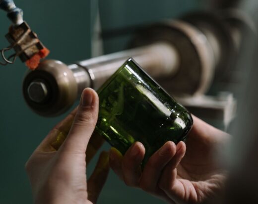 Handen inspecteren een groene glazen fles bij een werkbank