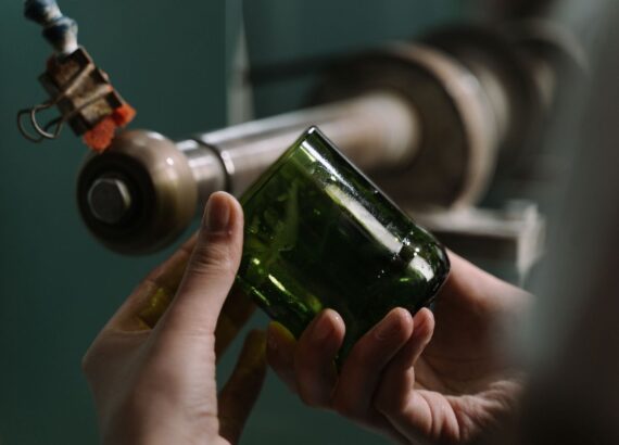 Handen inspecteren een groene glazen fles bij een werkbank