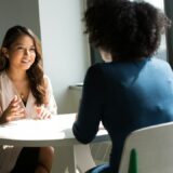 Twee medewerkers voeren een gesprek aan een tafel in een lichte ruimte