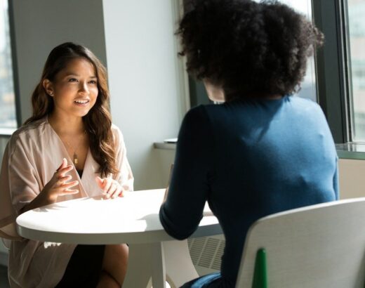 Twee medewerkers voeren een gesprek aan een tafel in een lichte ruimte