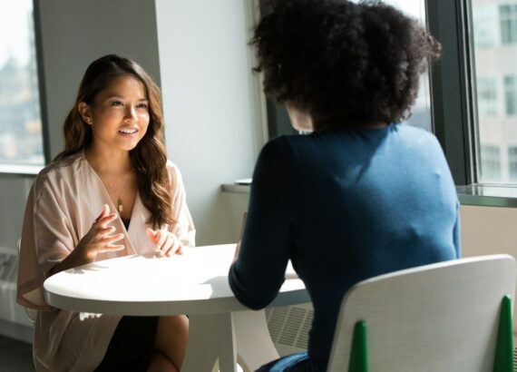 Twee medewerkers voeren een gesprek aan een tafel in een lichte ruimte
